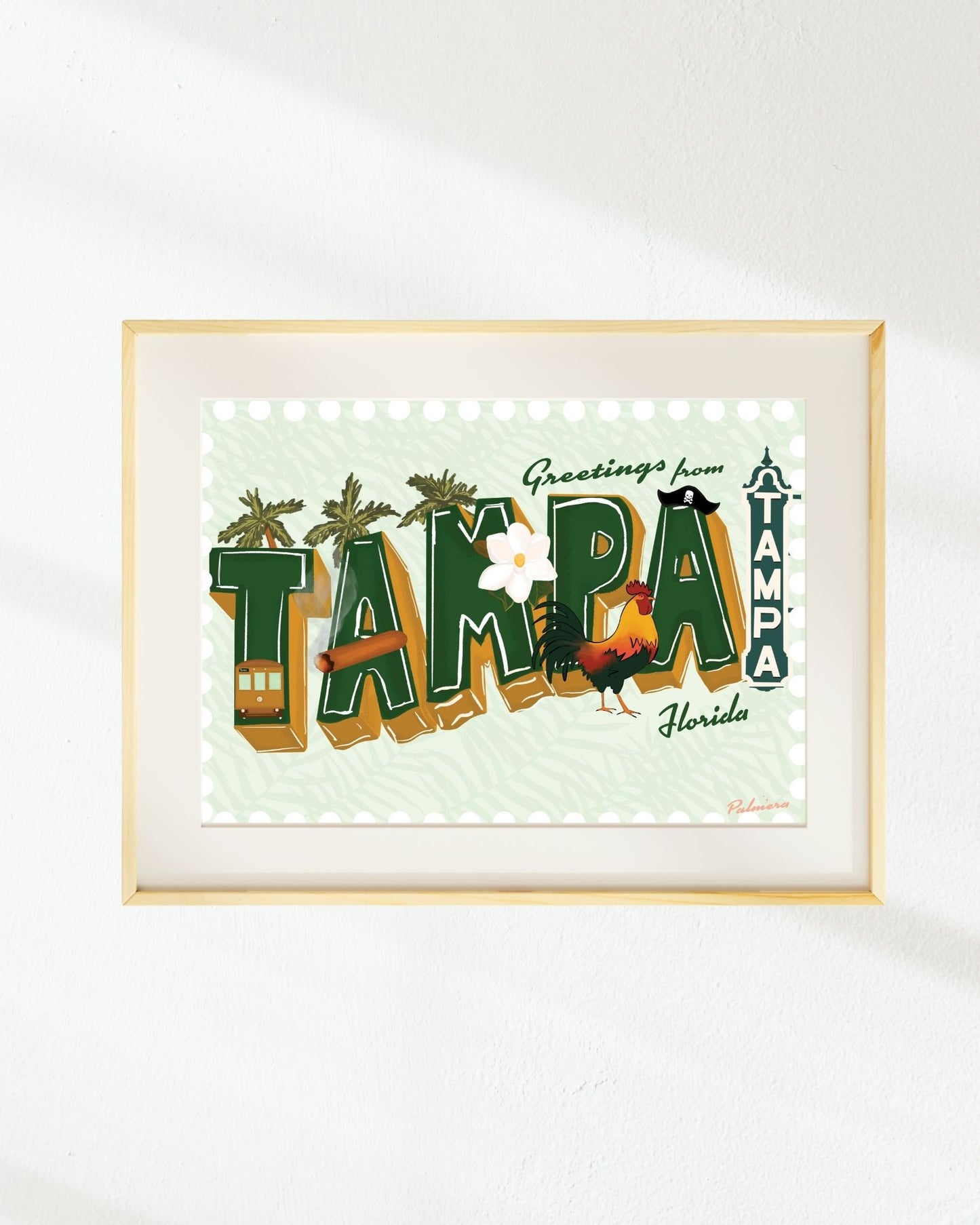 Framed art print featuring a retro-style 'Greetings from Tampa, Florida' design with illustrated palm trees, a trampoline, a rooster, and a small bus, displayed on a white wall.