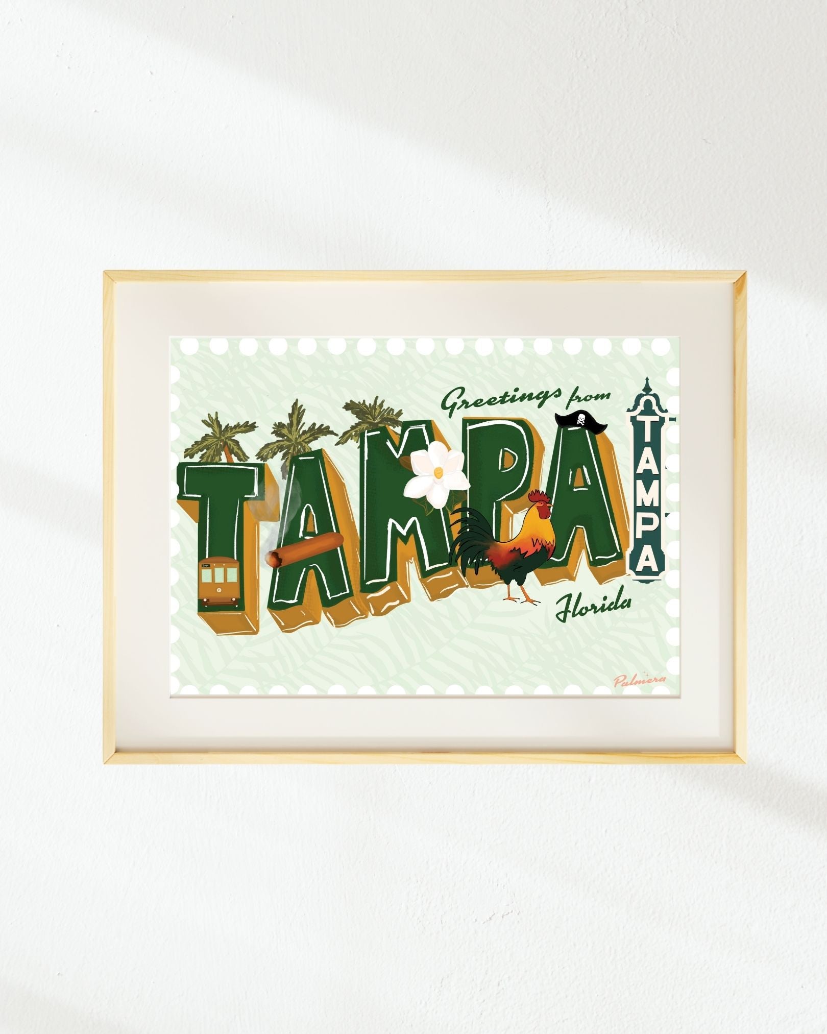 Framed art print featuring a retro-style 'Greetings from Tampa, Florida' design with illustrated palm trees, a trampoline, a rooster, and a small bus, displayed on a white wall.