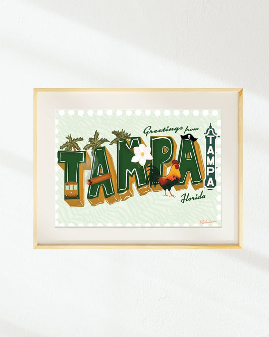 Framed art print featuring a retro-style 'Greetings from Tampa, Florida' design with illustrated palm trees, a trampoline, a rooster, and a small bus, displayed on a white wall.